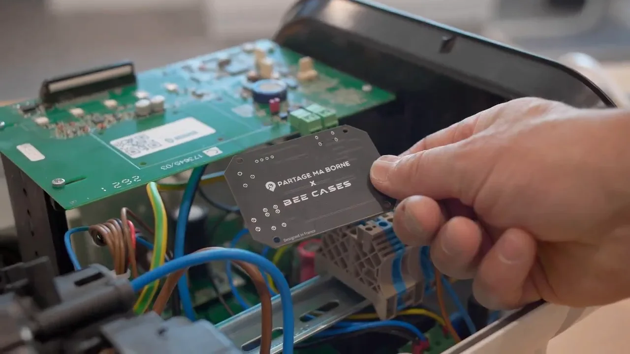 Carte électronique Partage Ma Borne x Bee-Cases tenue devant une borne de recharge ouverte